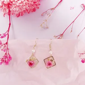 Detalle de pendientes hechos a mano con flores secas rosas y pan de oro en resina