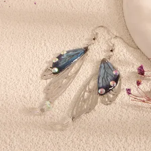 Close-up detail view of cicada wing earrings with blue resin and iridescent crystals