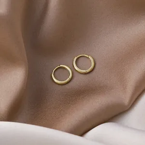 Macro detail of minimalist small gold hoop earrings on soft satin background