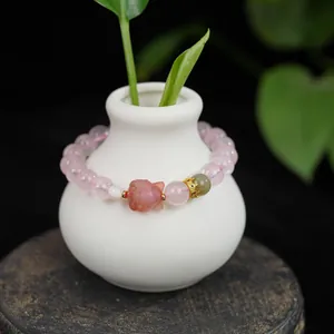 Detailed shot of a natural pink crystal bracelet with a carved fox and crown charm