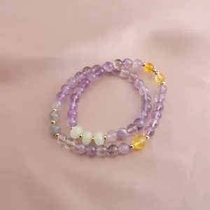 Close-up of elegant double-layered amethyst and citrine beaded bracelet on pink silk.