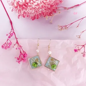 Detalle de pendientes cuadrados de resina con flores secas reales y láminas de oro