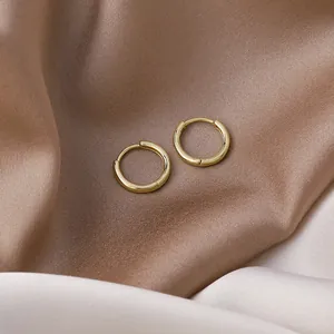Macro detail of polished gold minimalist hoop earrings on draped satin fabric background.