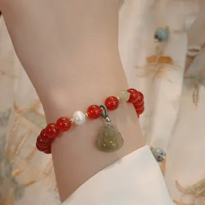 Nahaufnahme eines roten Achat-Armbands mit geschnitztem grünem Jade-Buddha-Anhänger.