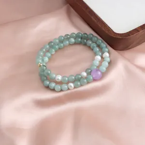 Close-up detail of a double-layer jadeite and pearl beaded bracelet on pink satin