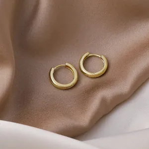 High-quality close-up of minimalist gold geometric hoop earrings on elegant satin fabric