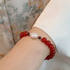 Detail eines Armbands aus rotem Achat mit zentraler weißer Perle und Granatakzenten.