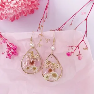 Primer plano de pendientes de resina con flores secas reales, perlas y pan de oro