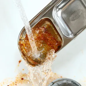 Detail of stainless steel seasoning dish being rinsed under running water for easy cleaning.
