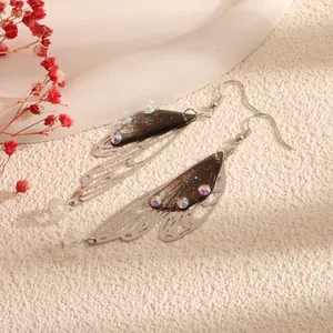 Detailed view of fashionable butterfly wing earrings with rhinestones on warm background.