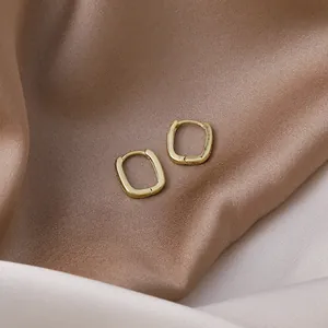 Close-up detail of minimalist gold geometric rectangular hoop earrings on silk fabric backdrop