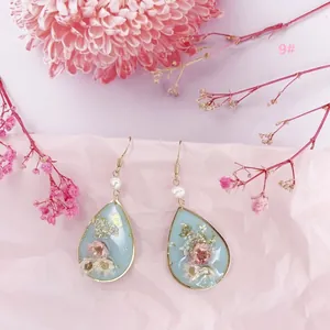 Vista de detalle de pendientes de resina en forma de gota con flores secas y perlas.