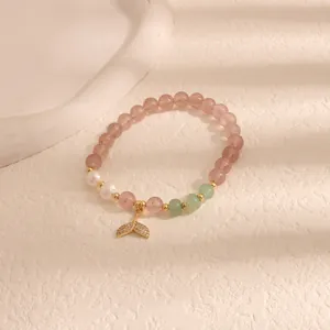 Dettaglio macro di un braccialetto di perle di quarzo rosa con ciondolo a sirena.