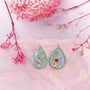 Detalle de pendientes de resina en forma de gota con flores secas reales y pan de oro.