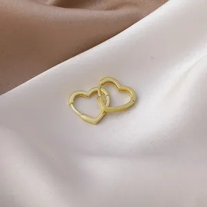 Detail shot of minimalist gold heart-shaped hoop earrings on elegant silk background