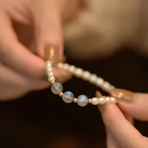Detail view of rice freshwater pearl and iridescent moonstone beaded elastic bracelet on hand