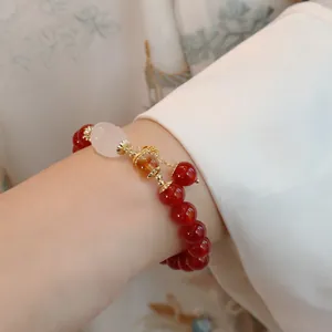 Detail eines roten Achat-Armbands mit weißem Jade-Buddha und goldenen Anhängern