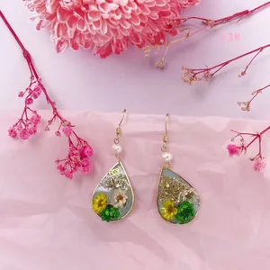 Primer plano de pendientes de gota con flores secas reales y detalles en pan de oro