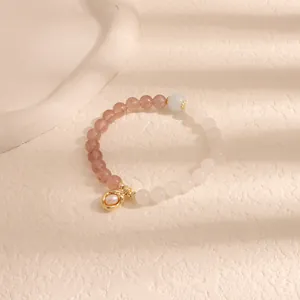 Dettaglio di un braccialetto di perline con pietre rosa e bianche e ciondolo dorato