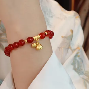 Detailansicht eines Armbands aus rotem Achat mit goldenen Lotusanhängern am Handgelenk.