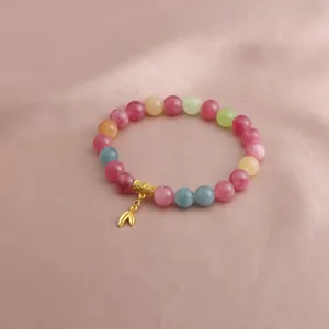 Detail des bunten Turmalin-Perlenarmbands mit goldenem Anhänger auf rosa Seide
