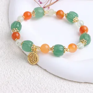 Nahaufnahme eines Perlenarmband im Ethno-Stil mit grünen Kürbis-Jadesteinen und Goldanhänger