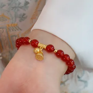 Detailansicht eines Armbands aus rotem Achat mit kunstvollen goldenen Lotoskapsel-Anhängern