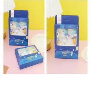 Detail shot of astronaut and rocket cake candles in a blue windowed gift box packaging.