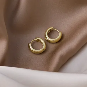 Macro view of minimalist gold hoop earrings on soft champagne silk fabric.