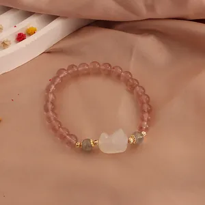 Detail view of strawberry crystal bracelet with a moonstone cat claw charm on pink fabric