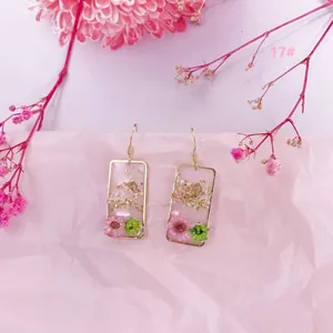 Primer plano de pendientes geométricos hechos a mano con flores secas reales y pan de oro
