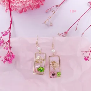 Primer plano de pendientes rectangulares hechos a mano con flores secas reales, pan de oro y perlas