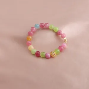 Nahaufnahme eines bunten Turmalin-Perlenarmbands mit goldenem Lotus-Anhänger auf Satin.