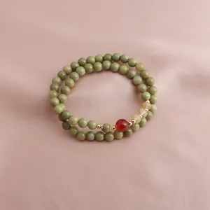 Detailed macro view of a double-strand avocado green stone bracelet with red and amber beads.