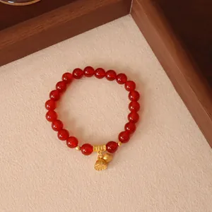 Makroaufnahme eines roten Achat-Armbands mit exquisitem goldenem Lotuskapsel-Anhänger