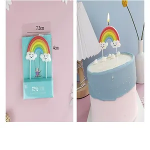 Detail view of a lit rainbow and cloud birthday candle topper on a decorative cake