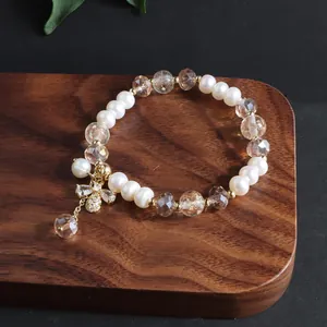 Nahaufnahme eines Süßwasserperlenarmbands mit goldenem Bienenanhänger auf Holzdekor.