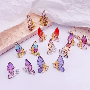 Primer plano de pendientes de alas de mariposa 3D con circonitas sobre fondo de piedra.
