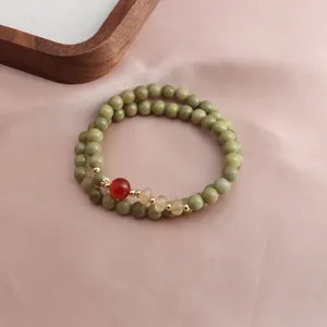 Close-up of a double-strand green stone bracelet with red and yellow accents on pink satin
