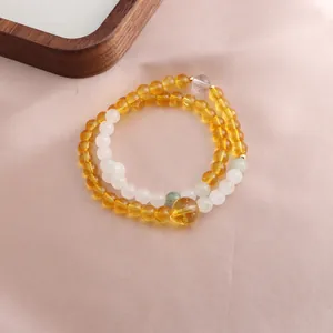 Macro detail of a double-strand citrine and white gemstone beaded bracelet on pink silk.