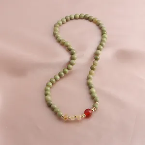 Detailed close-up view of avocado green Alxa stone beads with red and gold accents on pink silk