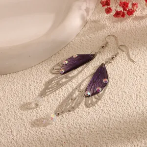 Detailed view of purple cicada wing earrings with iridescent rhinestones on white texture.