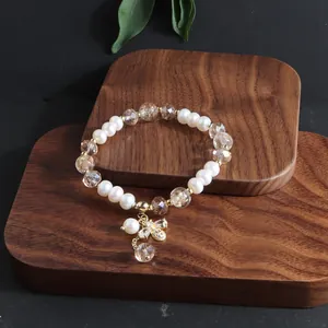 Detailansicht eines Perlen- und Kristallarmbands mit goldenem Bienenanhänger auf Holz