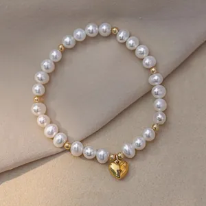 Détail d'un élégant bracelet en perles d'eau douce avec pendentif cœur doré sur tissu beige