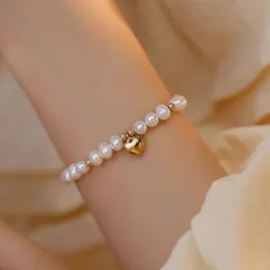 Gros plan d'un élégant bracelet en perles d'eau douce avec un pendentif cœur doré au poignet