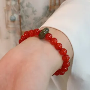 Detailansicht eines Armbands aus rotem Achat mit Hetian-Jade-Anhänger am Handgelenk
