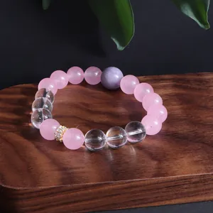 Nahaufnahme eines minimalistischen Armbands aus Rosenquarz und Kristall auf Holztablett