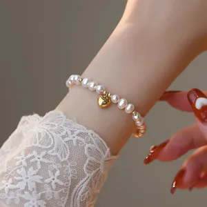Détail d'un élégant bracelet en perles d'eau douce avec un charmant cœur doré au poignet