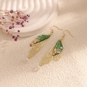 Detailed shot of green wing-shaped drop earrings with crystals and gold filigree