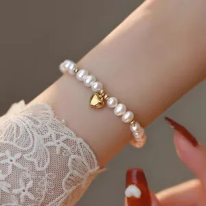 Gros plan d'un élégant bracelet en perles d'eau douce avec un pendentif en cœur doré au poignet